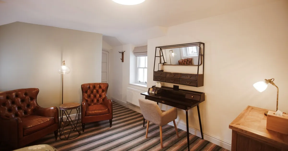 Cosy home office with brown leather armchairs, a dark writing desk and striped carpet.