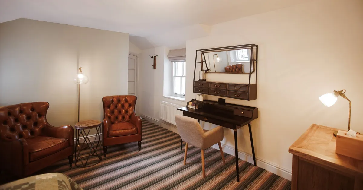 Cosy home office with brown leather armchairs, a dark writing desk and striped carpet.