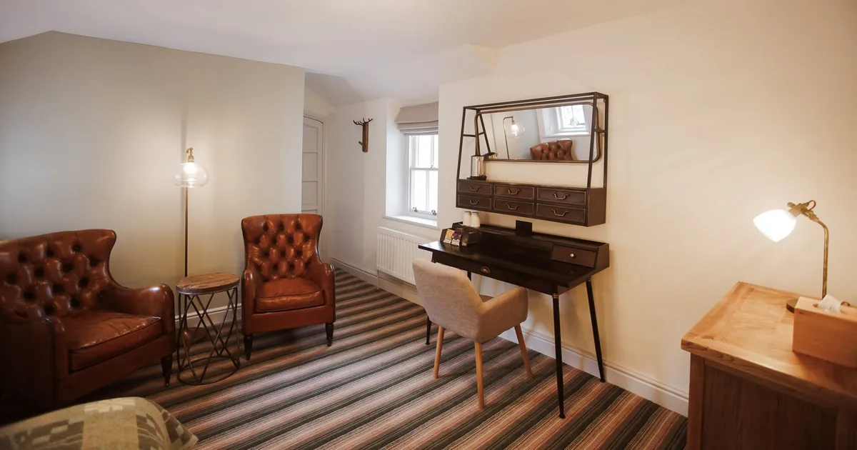 Cosy home office with brown leather armchairs, a dark writing desk and striped carpet.