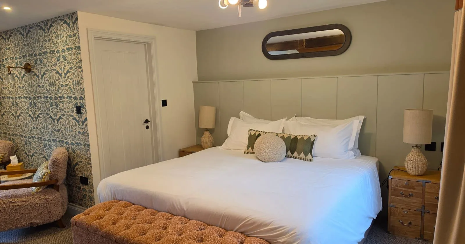 Cosy boutique bedroom with a large bed, patterned feature wall and upholstered bench.
