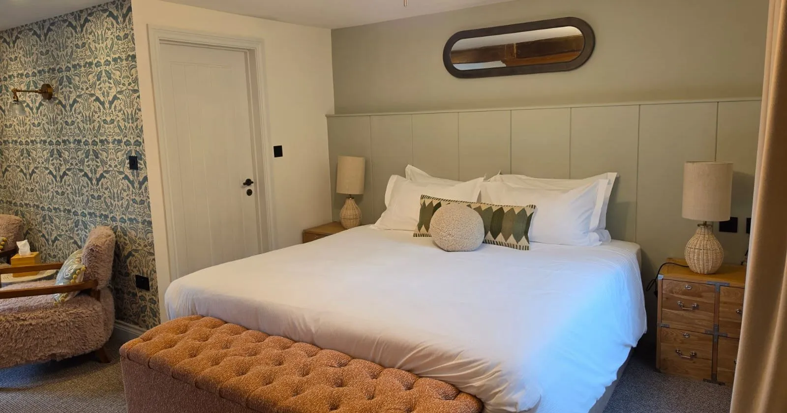Cosy boutique bedroom with a large bed, patterned feature wall and upholstered bench.