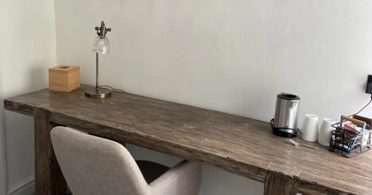 Cosy workspace with a rustic wooden desk, upholstered chair and framed mountain lake artwork.