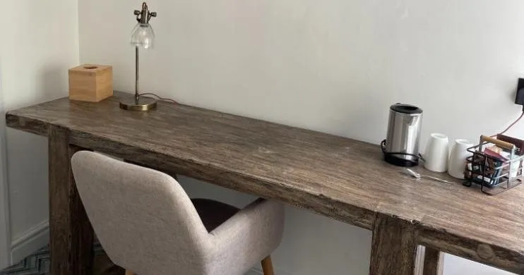 Cosy workspace with a rustic wooden desk, upholstered chair and framed mountain lake artwork.