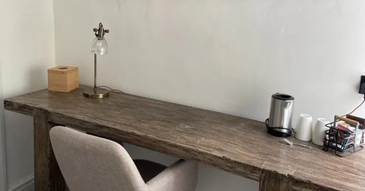Cosy workspace with a rustic wooden desk, upholstered chair and framed mountain lake artwork.