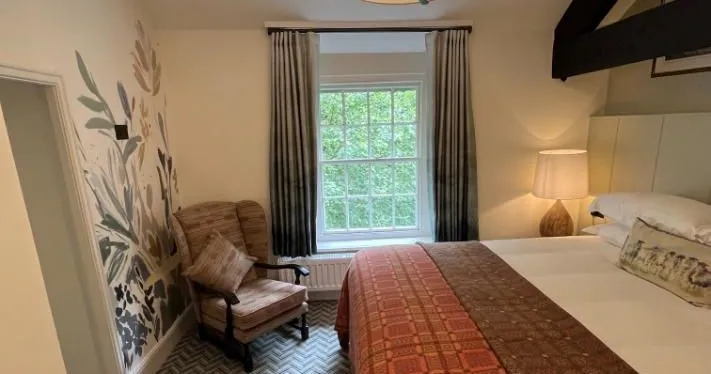 Cosy bedroom with a double bed, patterned throw, armchair and botanical wall mural.