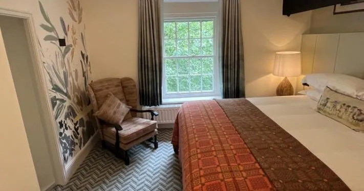Cosy bedroom with a double bed, patterned throw, armchair and botanical wall mural.