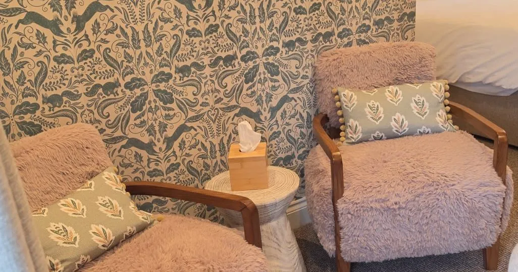 Cosy bedroom seating nook with two faux-fur armchairs, patterned wallpaper and a small side table.