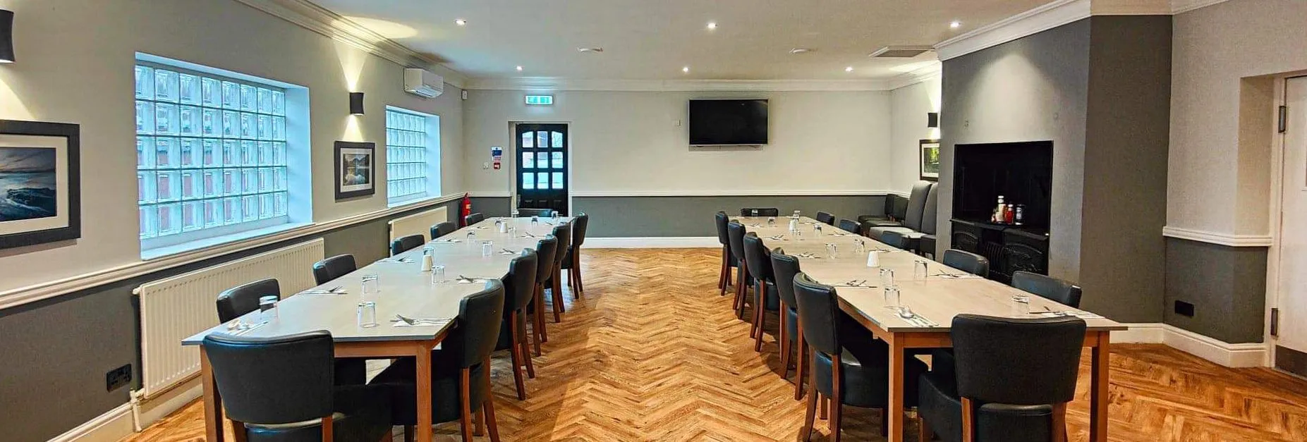 Modern conference room with two long tables and several chairs arranged in a U-shape.