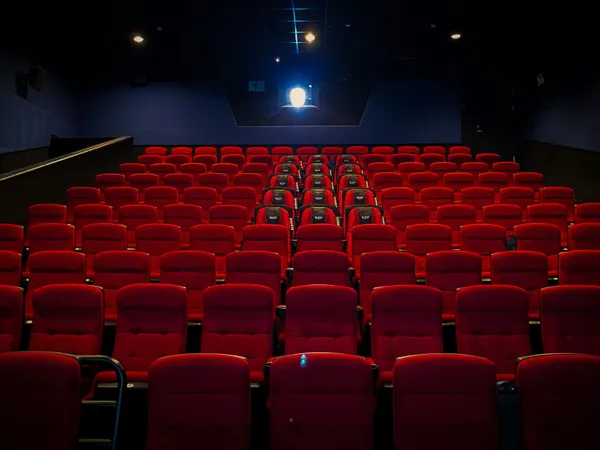 Empty cinema hall with rows of red seats and a lit projector at the back