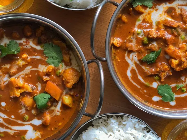 Indian curry dishes with white rice and drinks on a wooden tray