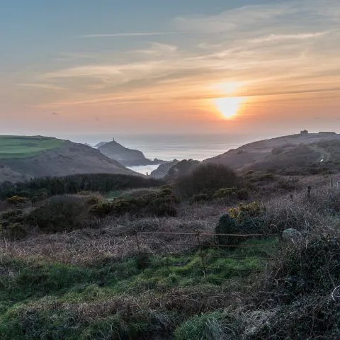 Sunset over Kenidjack Valley with the sun shining over rolling hills and the sea in the distance.