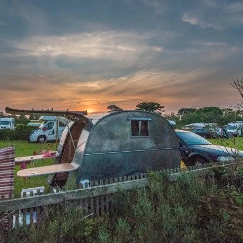 Teardrop trailer parked at a campsite at sunset with cars and other tents in the background