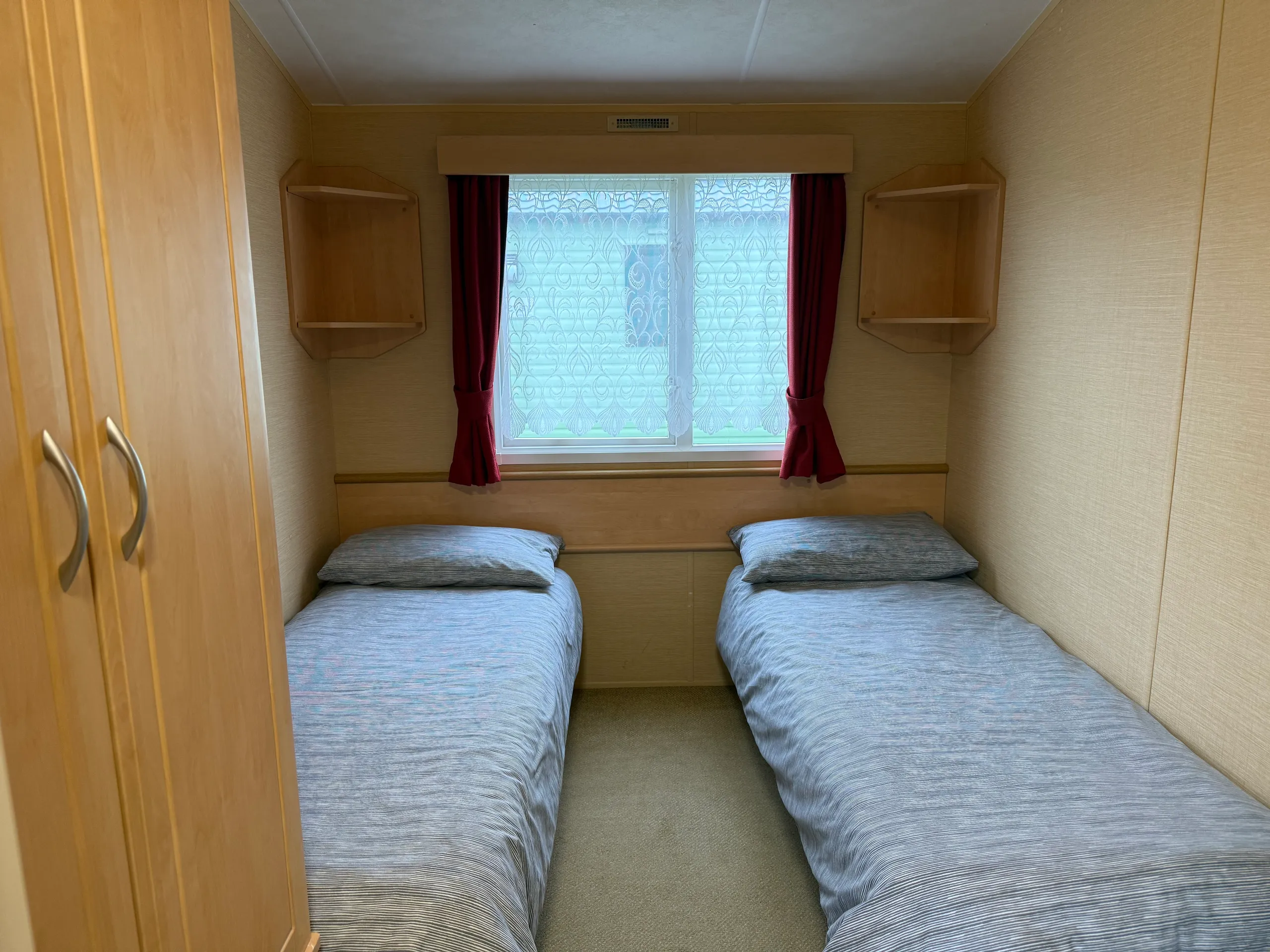Small bedroom with two single beds and a window with red curtains