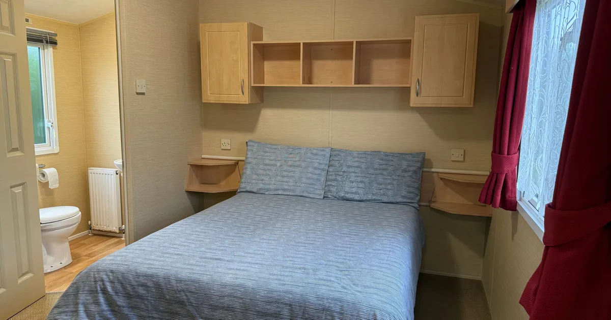 Small bedroom with double bed, attached bathroom, and red curtains