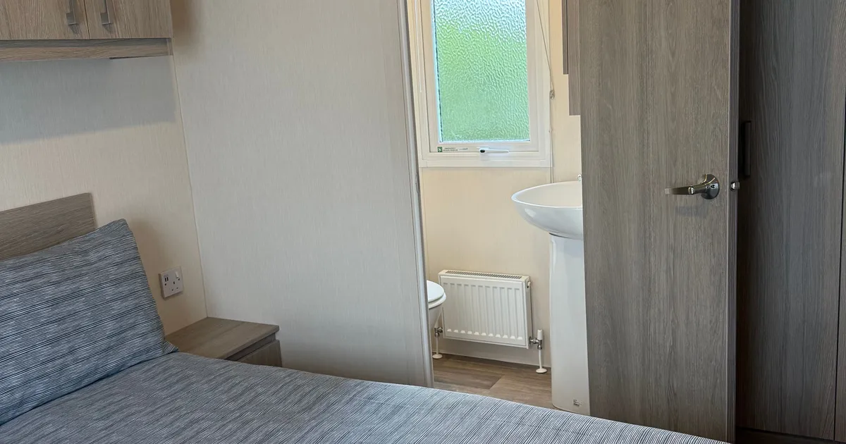 A modern bedroom with a neatly made bed and an open door revealing a small bathroom.