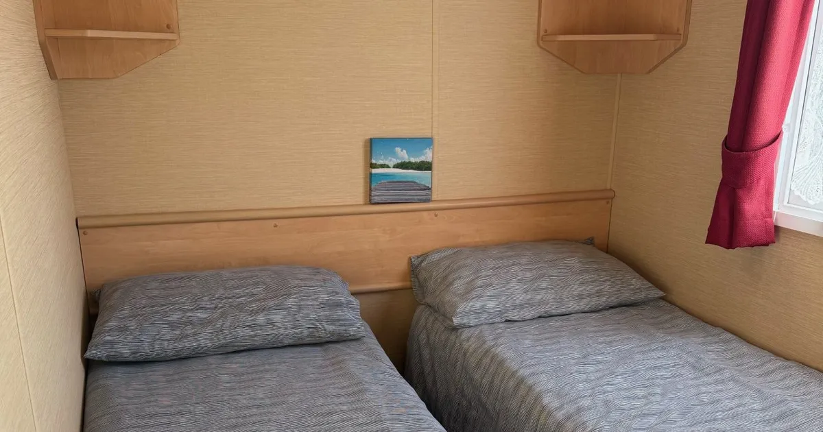 Small bedroom with two single beds, light wood shelves, and a window with red curtains.