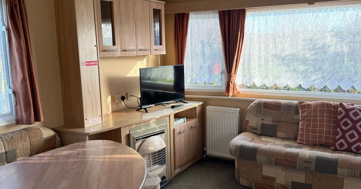 Cozy caravan living area with patterned sofas, a wooden dining table, TV, and large window with sheer curtains.