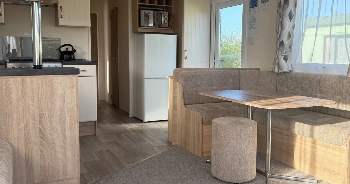 Modern mobile home interior with dining area, kitchen, and refrigerator.