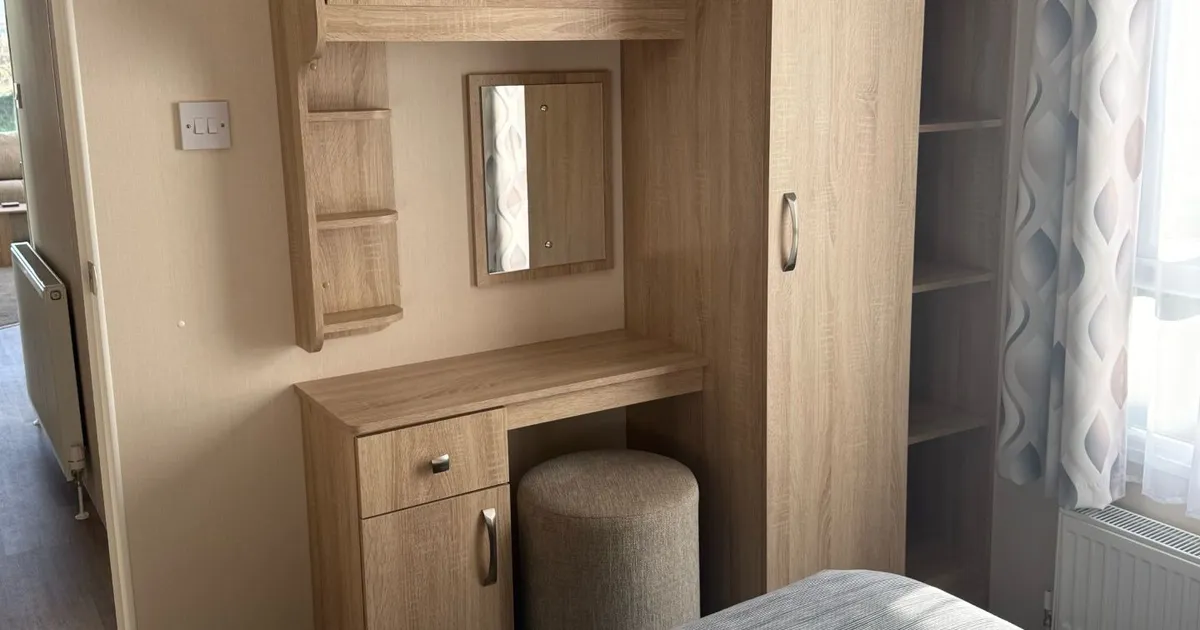 Wooden bedroom furniture set with storage, mirror, and stool near a window.