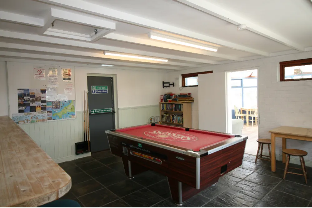 A recreational room with a pool table, bookshelf, tables, and stools.