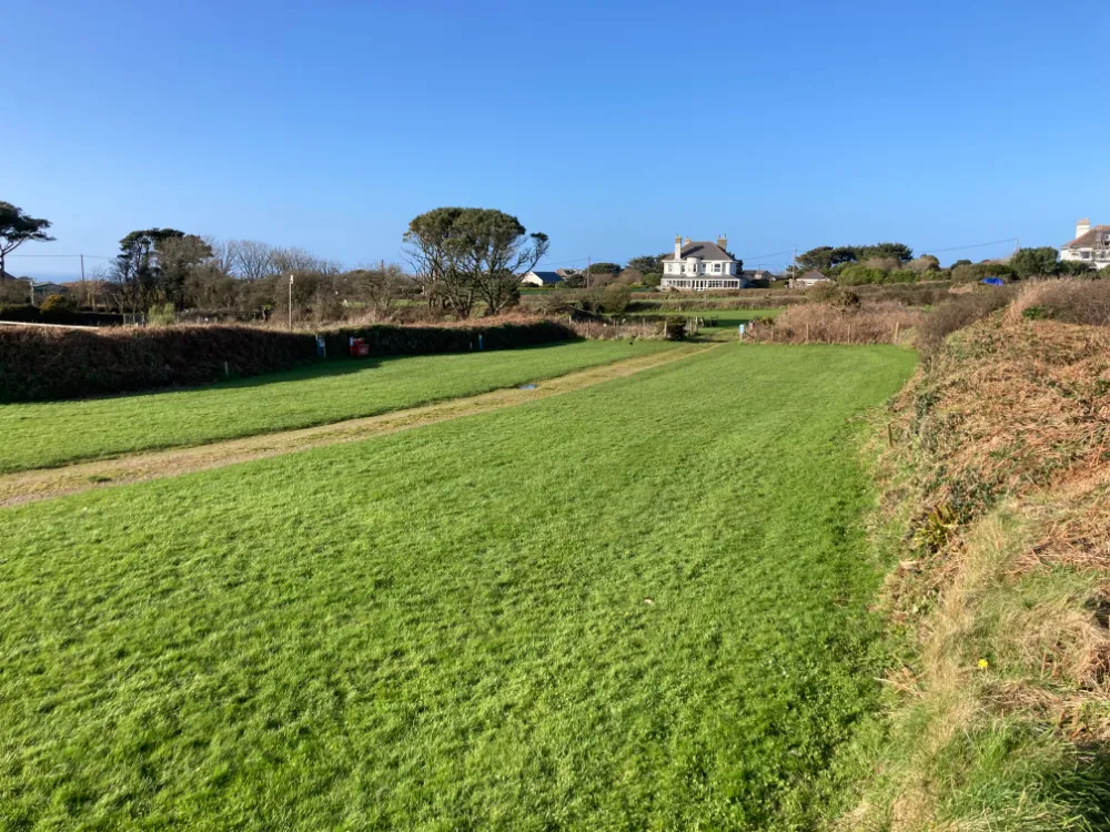 Grassy pitches with hedges and a house in the distance under a clear blue sky.