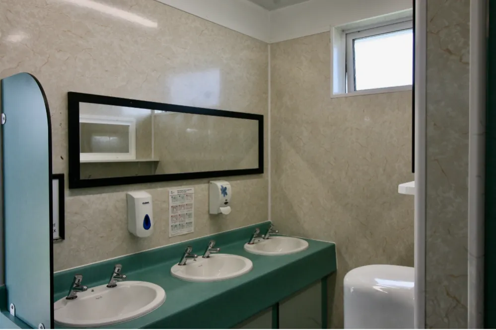 Public restroom with three sinks, soap dispensers, a rectangular mirror, and a small window.