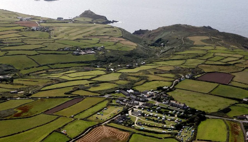 Aerial view of patchwork green fields, a coastal village, and the sea beyond.