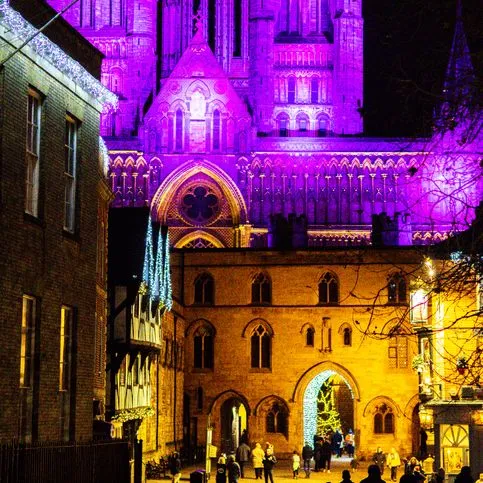 Gothic cathedral illuminated purple at night above a warmly lit street and archway