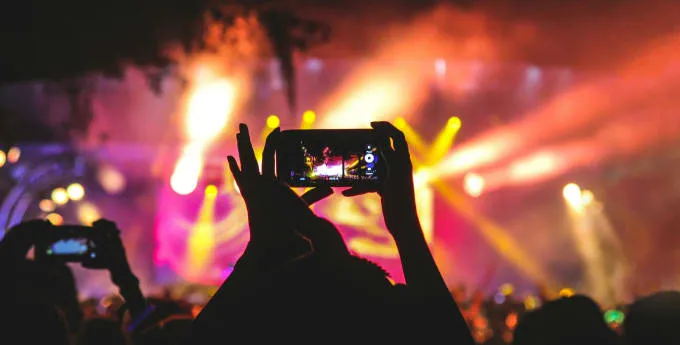 Audience at a concert capturing the colourful stage lights and performance with smartphones.