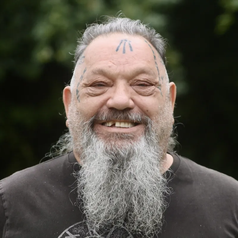 Smiling older man with facial tattoos and a long gray beard.
