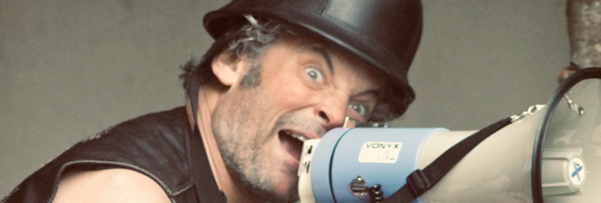 Man with a black helmet shouting into a megaphone