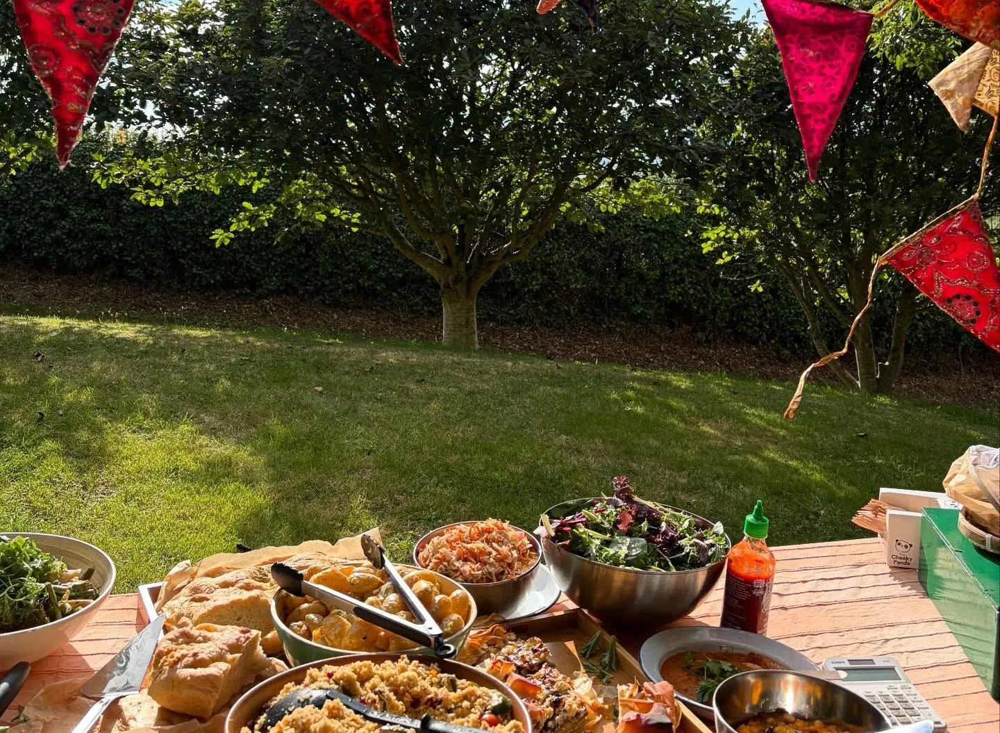 Outdoor picnic table with various dishes, under a canopy with colorful bunting flags.