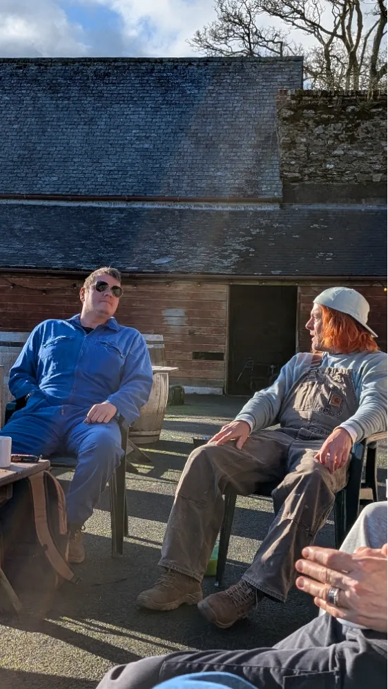 Two people sitting outside in casual work clothes, conversing and relaxing in the sun.
