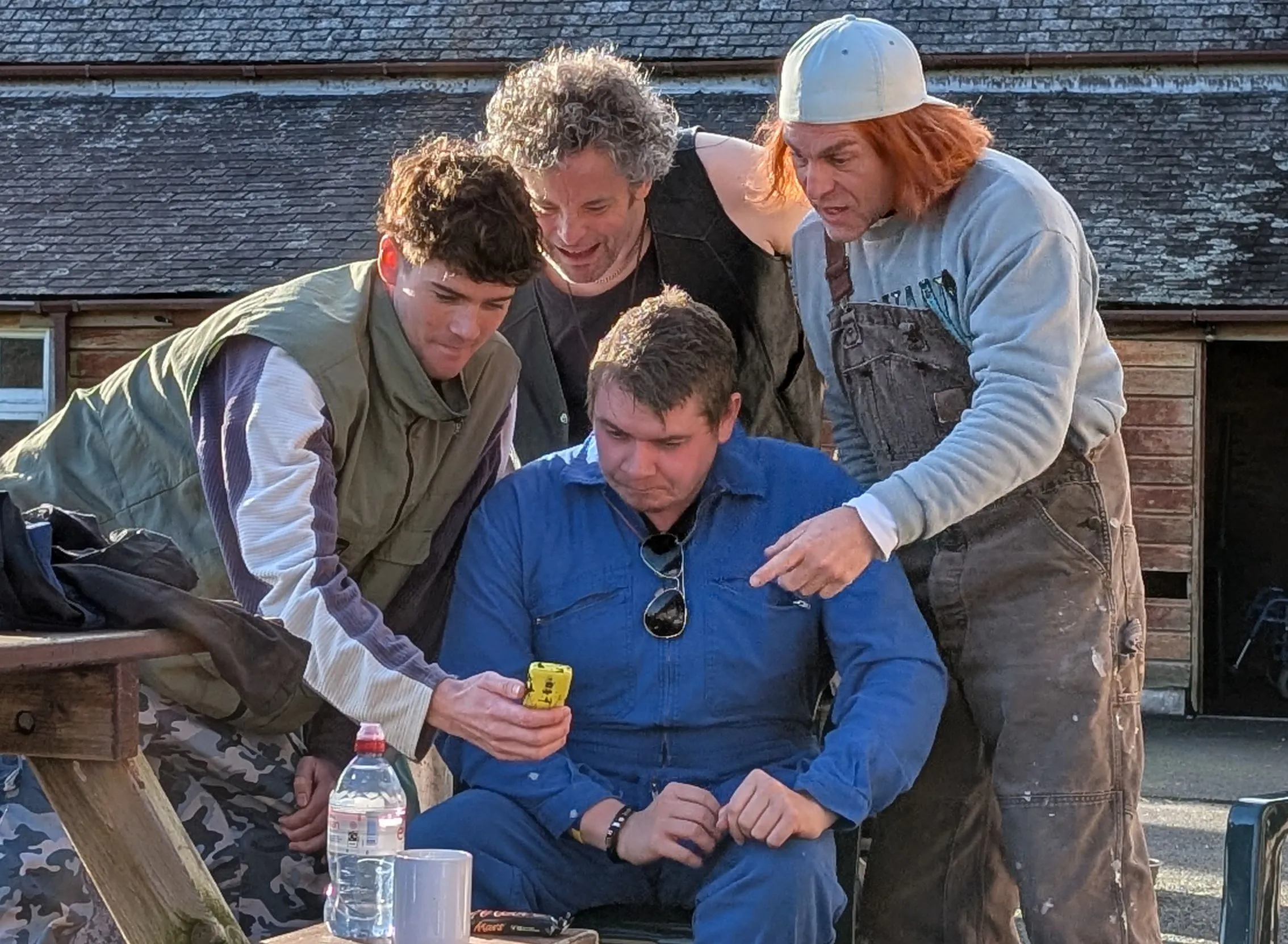 Four people gather and look intently at a yellow mobile phone outdoors.