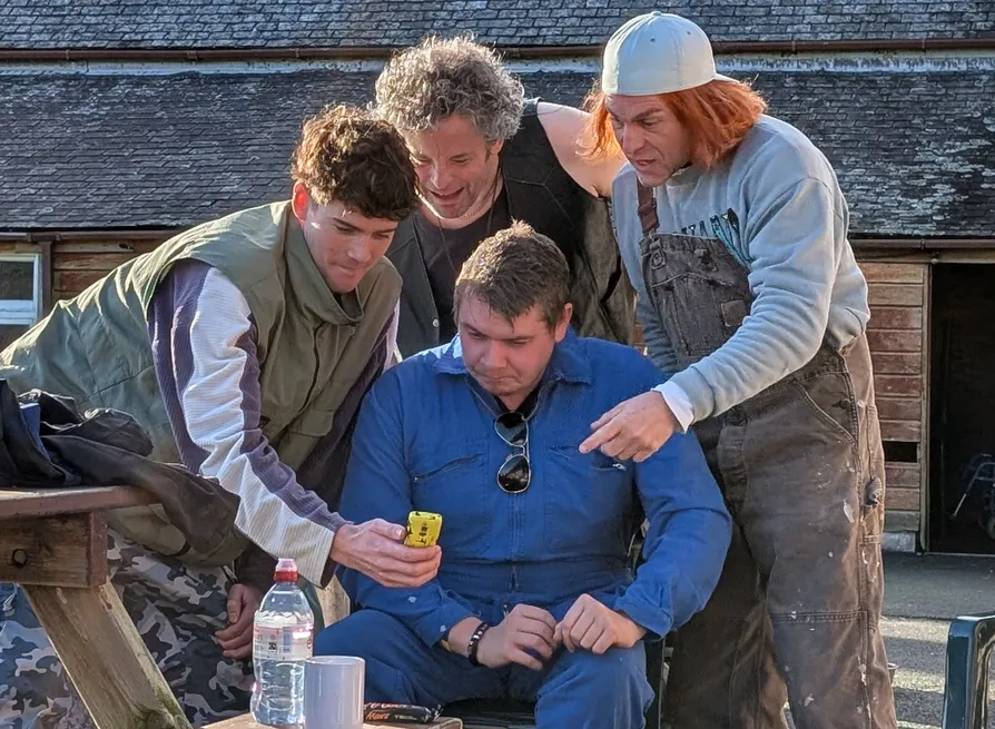 Four people gather and look intently at a yellow mobile phone outdoors.