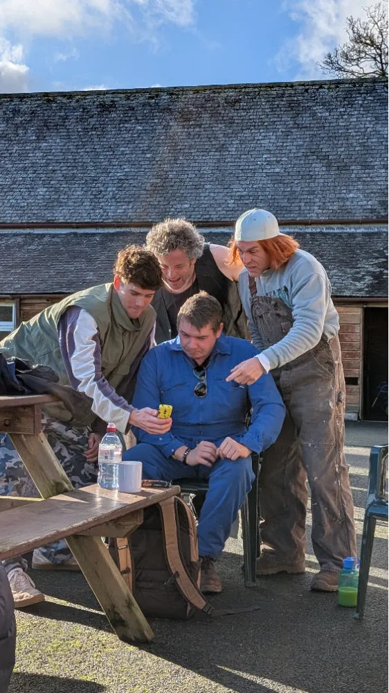 Four people gather and look intently at a yellow mobile phone outdoors.