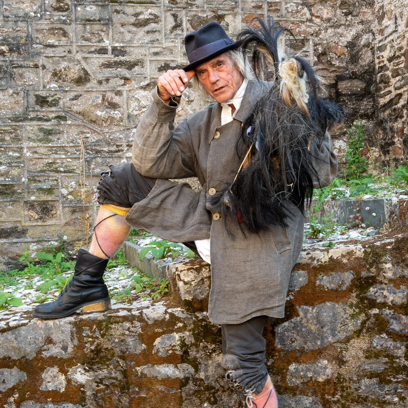 Man in traditional costume posing with one foot up on a stone wall