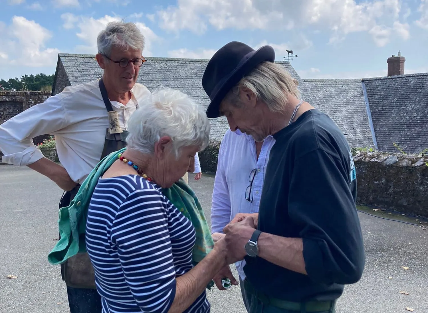 A group of older adults standing together outdoors, some holding hands and talking.