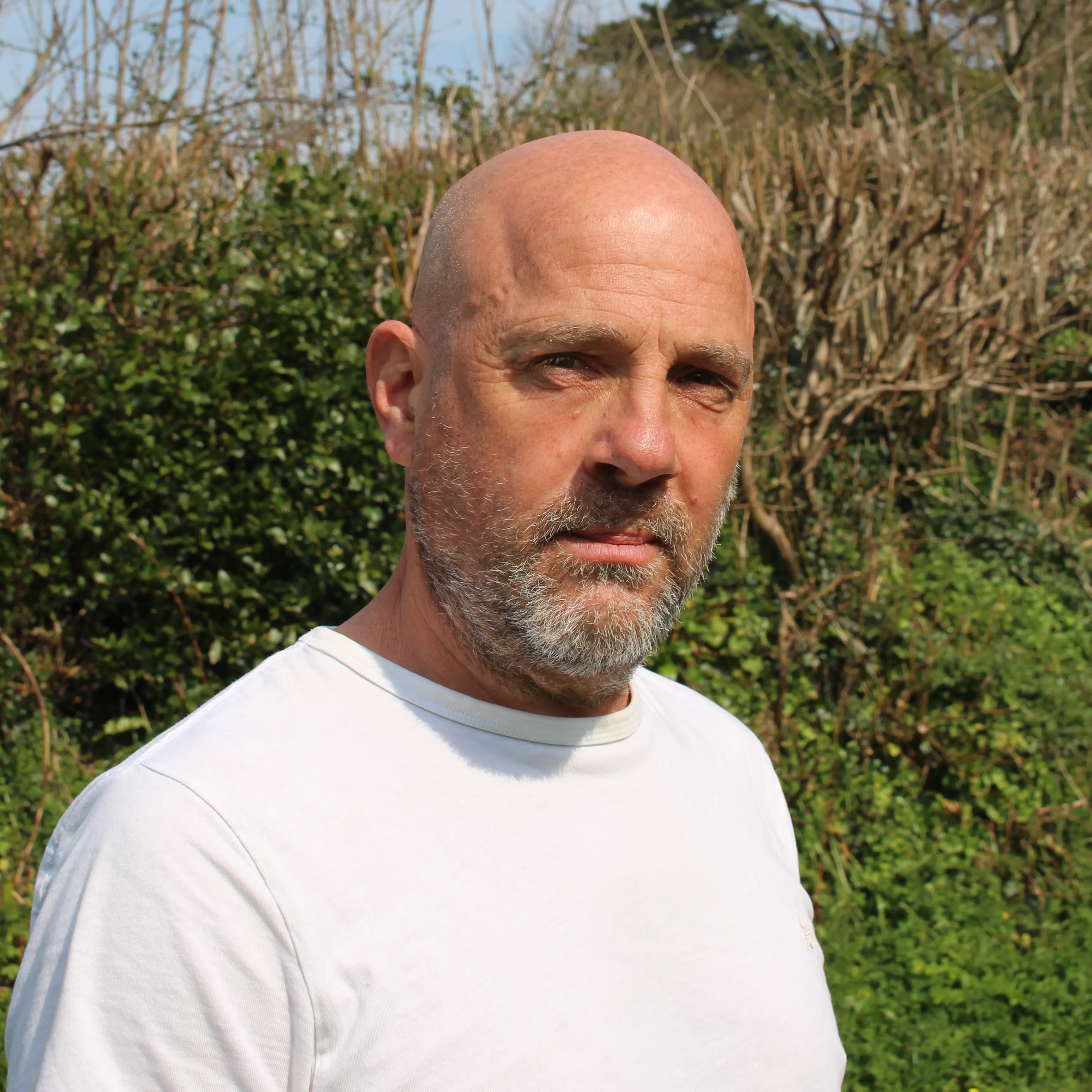 Bald man with beard wearing white shirt standing outdoors