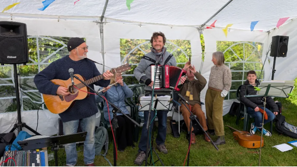 A group of people playing musical instruments under a canopy outdoors.