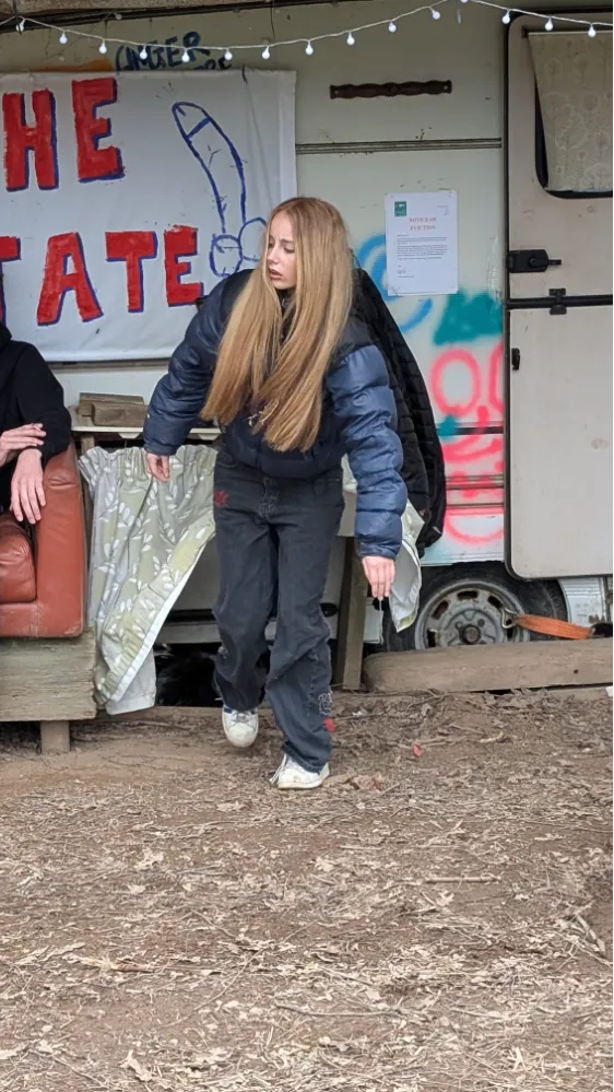 Person in dark clothing stepping outside a caravan with graffiti and eviction notice