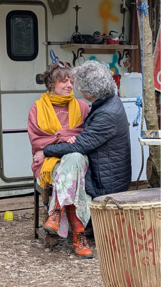 Two people sitting close together outdoors, sharing an intimate moment in front of a caravan, with one sitting on the other's lap.