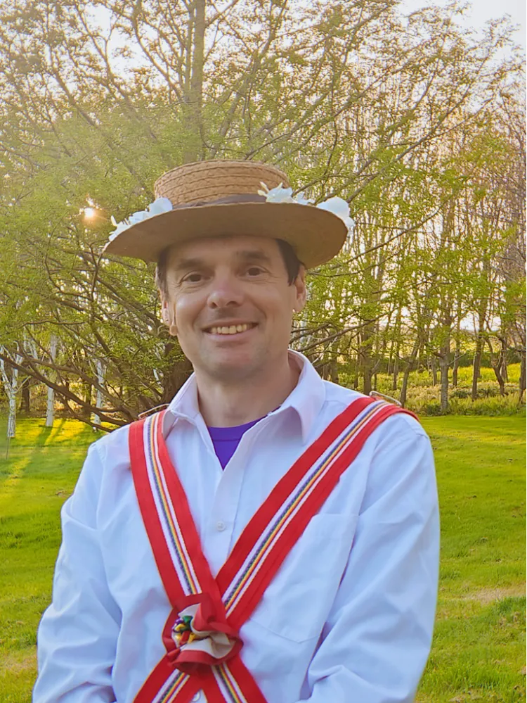 Man wearing traditional straw hat decorated with flowers and a white shirt with red and multicolored ribbons standing outside