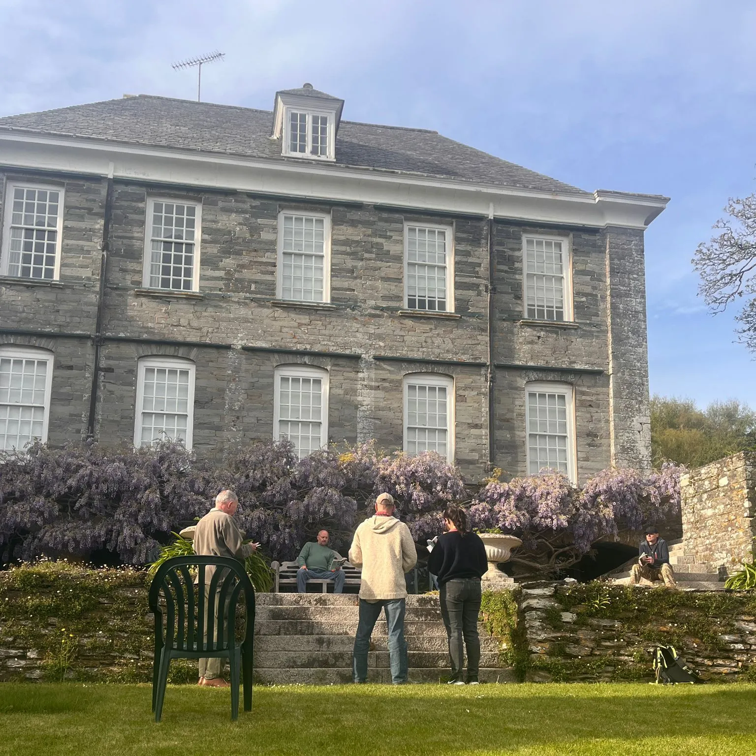 Cast members rehearse The Crucible on the lawn in front of a large stone house with blooming wisteria.