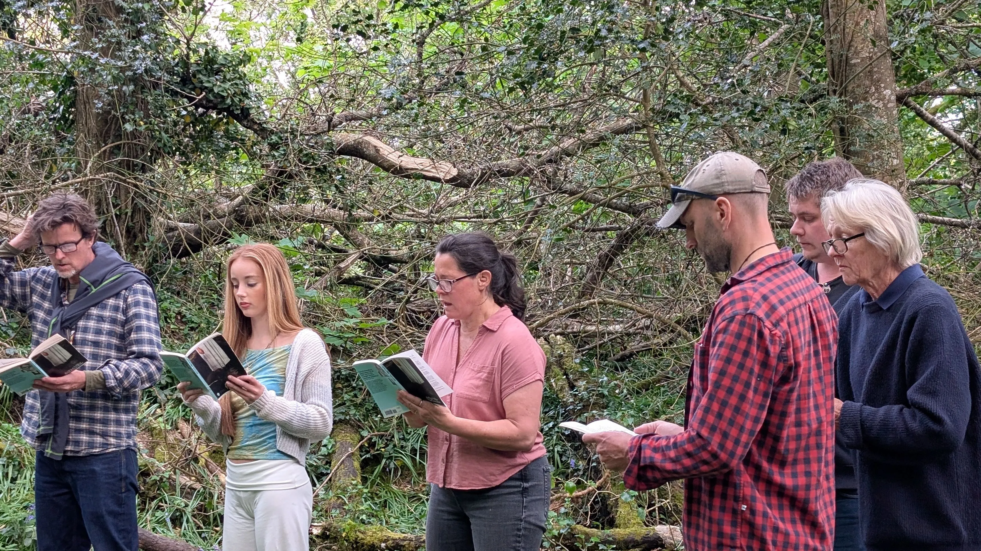 Cast members rehearse The Crucible outdoors in a wooded area, standing in a line and reading from scripts.