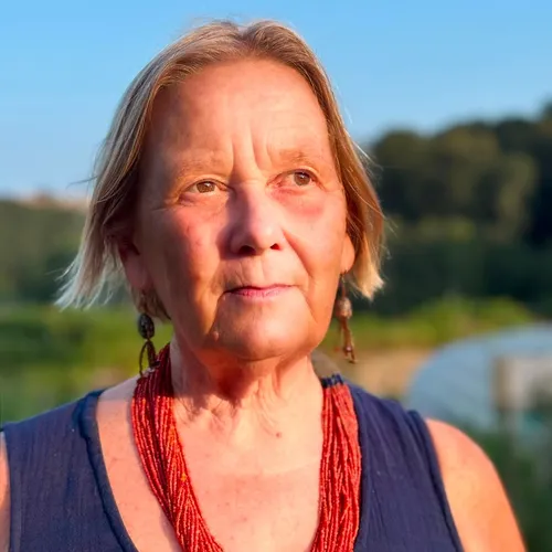 Portrait of Caroline McDougall outdoors in warm evening light, wearing a navy dress and layered red bead necklace.