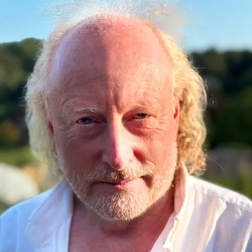 Portrait of Lord Montague Adrian Phippen outdoors in warm evening light, wearing a white open-collar shirt