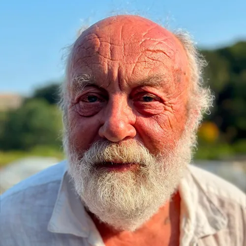 Close-up portrait of Prince Rob Heyland outdoors in warm sunlight, wearing a white shirt and sporting a full white beard.