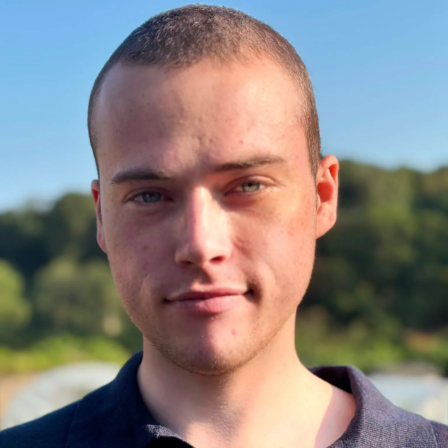 Portrait of Sampson Charlie Papenfus outdoors in natural sunlight, wearing a dark polo shirt