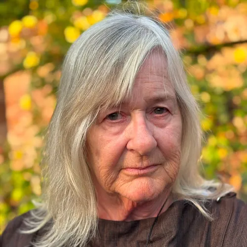 Portrait of an older woman with long grey hair outdoors against a softly blurred autumn background